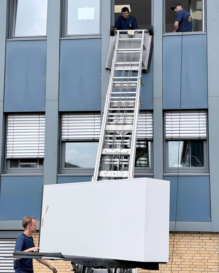 Ein Möbellift hebt einen großen Schrank an der Fassade eines Bürogebäudes nach oben